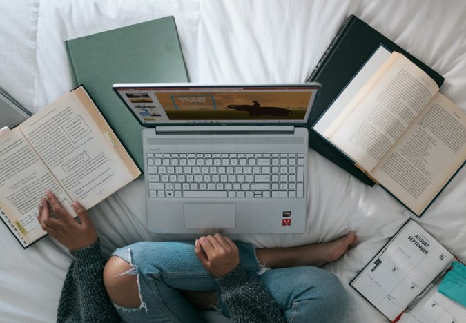 Girl studying on bed with laptop and books